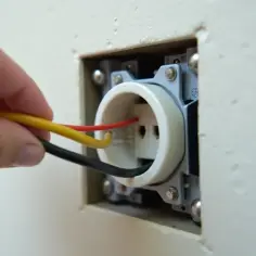Ręka podłącza przewody do gniazdka z uziemieniem. Widać żółty, czerwony i czarny kabel.