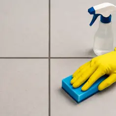 Ręka w żółtej rękawicy czyści niebieską gąbką fugi na balkonie. Dowiedz się, jak wyczyścić fugi na balkonie narażone na deszcz i mróz.