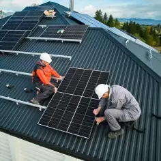 Dwóch monterów w kaskach pracuje nad instalacją PV na dachu. Montują panele słoneczne, przygotowując dom do produkcji czystej energii.