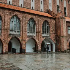 Zamek w Kwidzynie. W deszczowy dzień zwiedzający z parasolem podziwiają gotycką architekturę. Bilety do zamku warto kupić online.