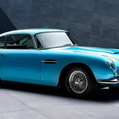 Błękitny Aston Martin DB5 z charakterystycznymi szprychowymi felgami, lśniącym chromem i kultową kratką chłodnicy.