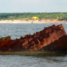 Rdza rdzy, wrak statku na Bałtyku. Czy to symbol tego, dlaczego wody bałtyku są znacznie zanieczyszczone? W tle plaża z ludźmi.