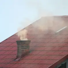 Dym z komina na czerwonym dachu. Warto zadbać o czystość, aby uniknąć problemów z tym, jak wypalić sadze w kominie.
