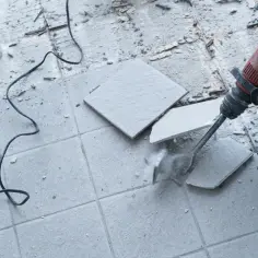 Młot udarowy usuwa stare płytki. Pokazuje to, jak skuć klej po płytkach, odsłaniając podłoże.