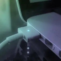 Ładowarka podłączona do laptopa z zapaloną niebieską diodą.