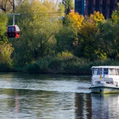 Polinka Wrocław trasa: dwie czerwone gondole kolejki linowej nad Odrą, obok płynie statek pasażerski.