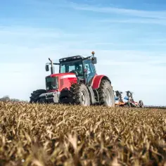 Czerwony traktor orze pole. Rolnicy pracują, a pytanie czy rolnicy płacą podatek od nieruchomości pozostaje otwarte.