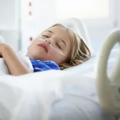 Dziecko śpi w szpitalnym łóżku z kaniulą tlenową. Lekarze kierują się zasadą "primum non nocere", dbając o jego dobro.