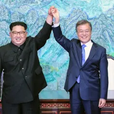 Kim Dzong Un, prezydent Korei Północnej, i Moon Jae-in pozdrawiają publiczność, trzymając się za ręce.