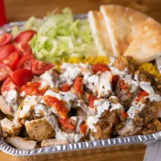 Pyszna shoarma z kurczaka z ryżem, pomidorami, sałatą i sosem, podana w aluminiowej tacce.