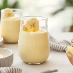 Kremowy koktajl z mango i bananem w szklance, obok świeże owoce.