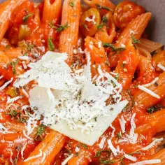 Penne w sosie pomidorowym z oliwkami i parmezanem. Idealny szybki obiad z makaronem, posypany świeżymi ziołami.