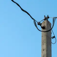 Betonowy słup energetyczny z przewodami na tle błękitnego nieba. Zastanawiasz się, ile wynosi odszkodowanie za słup energetyczny na działce?