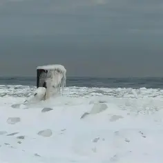 Zamarznięty słup na plaży, pokryty lodem, pokazuje, dlaczego morze zamarza zimą. Woda zamienia się w lód, tworząc zimowy krajobraz.