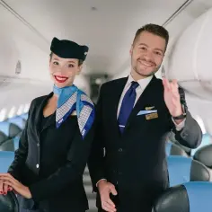 Uśmiechnięci steward i stewardessa LOT w uniformach, gotowi do lotu. Marzysz, jak zostać stewardessą? To może być Twój początek!