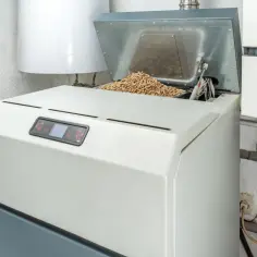 Piec na pellet z otwartą klapą zasypową wypełnioną pelletem.