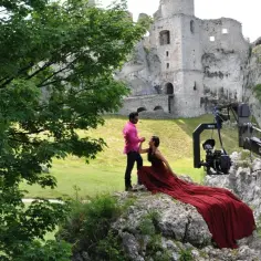 Scena z filmu "Nad Niemnem" kręcona w ruinach zamku. Para w strojach filmowych na tle kamiennych murów.