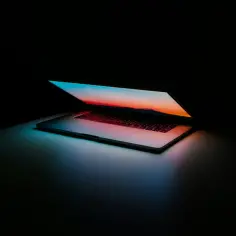 Laptop z podświetlaną klawiaturą i ekranem wyświetlającym zachód słońca. Dowiedz się, jak powiększyć ekran, by lepiej widzieć detale.