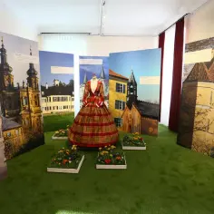 Suknia Sisi na tle wystawy z widokami pałaców i kościołów.