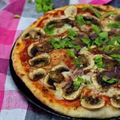 Domowa pizza z pieczarkami i cebulą, posypana świeżą natką pietruszki, na różowo-białej kratce.