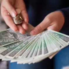 Dłonie liczą banknoty 100 zł i monety. Zastanawiasz się, jak sprawdzić lata pracy do emerytury?