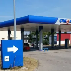 Stacja paliw CNG AUTO z niebieskim zadaszeniem i znakiem kierunkowym ze strzałką.