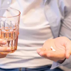 Mężczyzna trzyma szklankę wody i dwie białe tabletki, być może dutilox 30, gotowy do połknięcia.