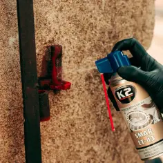 Ręka w czarnej rękawiczce aplikuje smar K2 LT-43 na metalowy element.