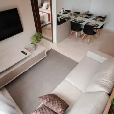 Nowoczesna suterena z salonem, jadalnią i sypialnią. Jasna kanapa, telewizor, stół z krzesłami.