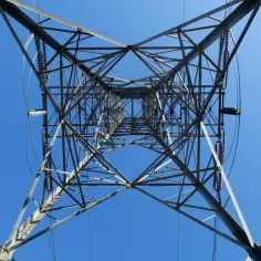 Widok z dołu na kratownicę stalową wieży energetycznej, przez którą biegnie linia średniego napięcia.