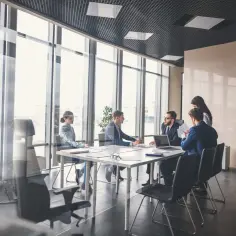 Grupa osób w garniturach dyskutuje przy stole w sali konferencyjnej. To spotkanie rady nadzorczej.