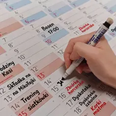 Planowanie **roku szkolnego**: ręka z markerem dopisuje wydarzenia do kalendarza: urodziny, treningi, dyskoteka szkolna.