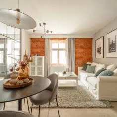 Nowoczesny salon z ceglaną ścianą i białym narożnikiem. Zastanawiasz się, czy warto kupić mieszkanie pod wynajem? To może być świetna inwestycja.
