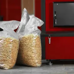 Dwie torby z pelletem drzewnym obok czerwonego pieca na pellet.