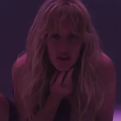 Ellie Goulding w klipie "Hate Me" z tekstem piosenki, w fioletowym świetle, z dłonią na podbródku.