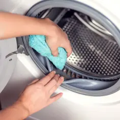 Czyszczenie uszczelki pralki zapobiega sytuacji, dlaczego pralka brudzi ubrania. Ręce wycierają gumę.