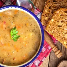 Aksamitna zupa grochowa, przepis babci, z kawałkami wędzonki i natką pietruszki. Podana z chlebem żytnim na drewnianym stole.