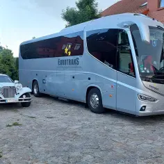 Szary autokar Eurotrans i biała limuzyna stoją na brukowanym dziedzińcu. Dowiedz się, ile kosztuje wynajem autokaru na podróż.
