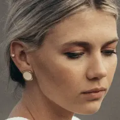 Delikatny kolczyk w chrząstce ucha, ozdobiony małym kamieniem, nie musi boleć. Kobieta z dwoma kolczykami na uchu.