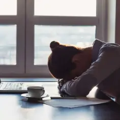 Zmęczona osoba z głową na biurku obok laptopa i kawy. Czy bezpośrednie zanoszenie CV do firmy wciąż działa na rynku?