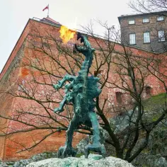 Smok Wawelski zieje ogniem przed ceglanym murem Wawelu w Krak.