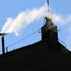 Biały dym z komina, jak sygnał wyboru nowego papieża, unosi się na tle błękitnego nieba.