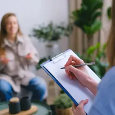 Psycholog notuje na kartce podczas rozmowy z pacjentką w gabinecie.