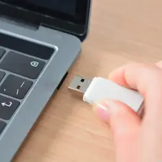 Dłoń wkłada pendrive do laptopa, przygotowując się do zapisania prezentacji Google na pendrive.