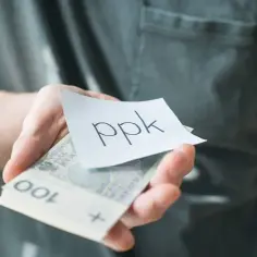 Dłoń trzyma plik banknotów i kartkę z napisem "ppk". Zastanawiasz się, ile można wpłacać na PPK?