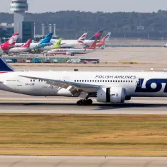 Samolot LOT Polish Airlines na płycie lotniska z innymi samolotami w tle.