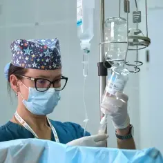 Pielęgniarka w maseczce i czepku z gwiazdkami przygotowuje kroplówkę. Czy pielęgniarka zarobki są adekwatne do jej pracy?