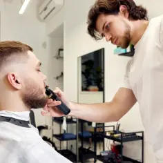 Barber precyzyjnie przycina brodę klienta. Zastanawiasz się, ile zarabia barber? To zależy od wielu czynników, ale umiejętności i doświadczenie są kluczowe.