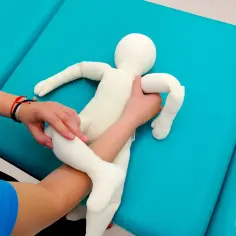 Instrukcja krok po kroku: jak podnosić noworodka. Dłoń podtrzymuje nóżki, druga ręka obejmuje tułów.