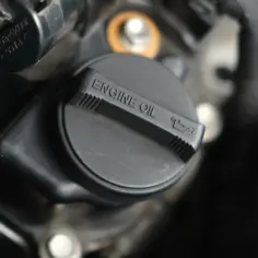 Czarny korek wlewu oleju silnikowego z napisem "ENGINE OIL" i ikonką. Pamiętaj o regularnej wymianie oleju, by silnik działał sprawnie.